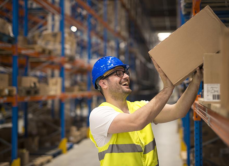 Smiling warehouse worker moving boxes on the shelf.